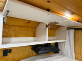 RV rental interior shows opened overhead cabinets, wood paneling, a mounted TV, and electrical outlets near the bed.