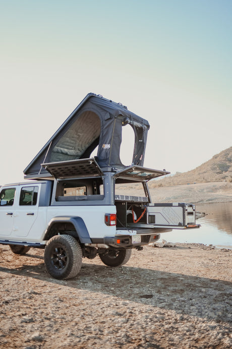 White Jeep Gladiator overland rig with a pop-up roof tent & pull-out fridge, ideal for an RV rental adventure by the lake.