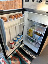 Open RV rental fridge, neatly packed with eggs, Waterloo sparkling water, Portland Sangria, and containers of food for the road.