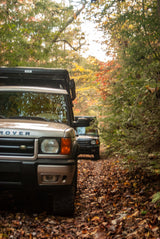 Two Land Rovers, one with a rooftop tent, on a leafy autumn trail. Perfect RV rental adventure.
