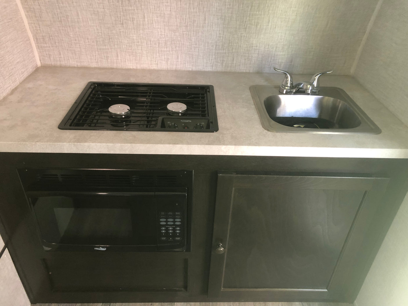 RV rental kitchen setup: sleek countertop with two-burner stove, stainless sink, microwave, and dark cabinets.