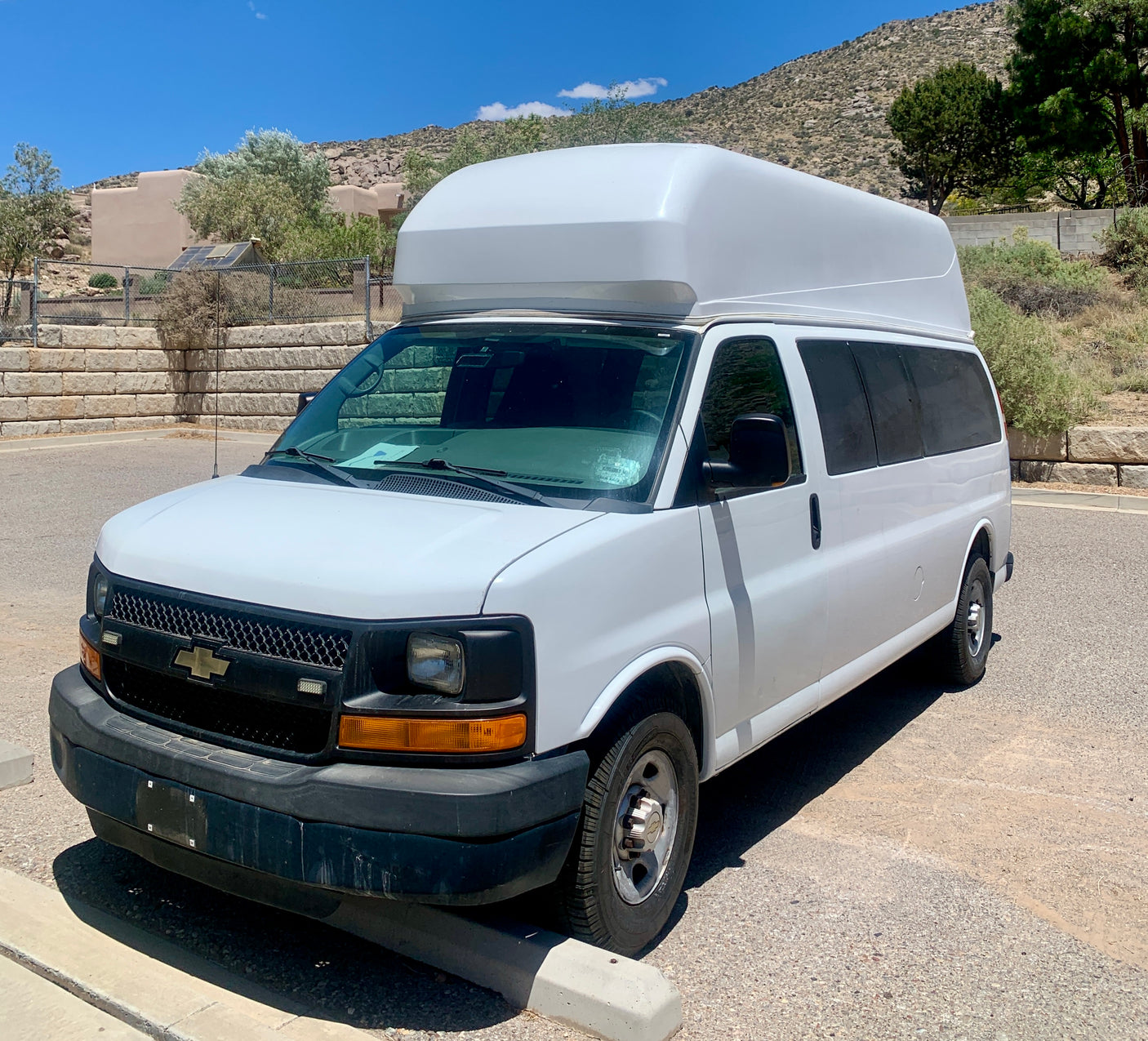 White high-roof Chevrolet van, a spacious option for rv rental, parked in a sunny, arid landscape with mountains.
