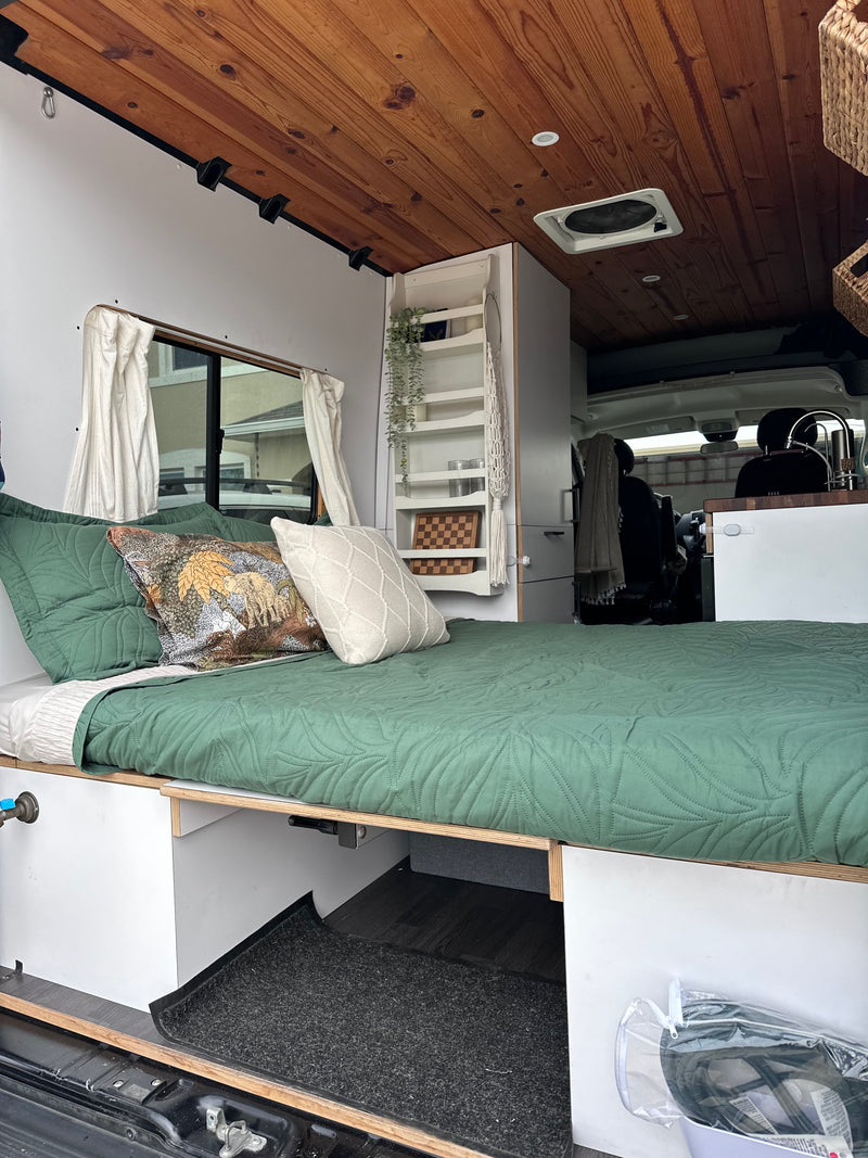 A comfortable RV rental interior with a green quilted bed, warm wood ceiling, and clever built-in storage for travel. — photo 2