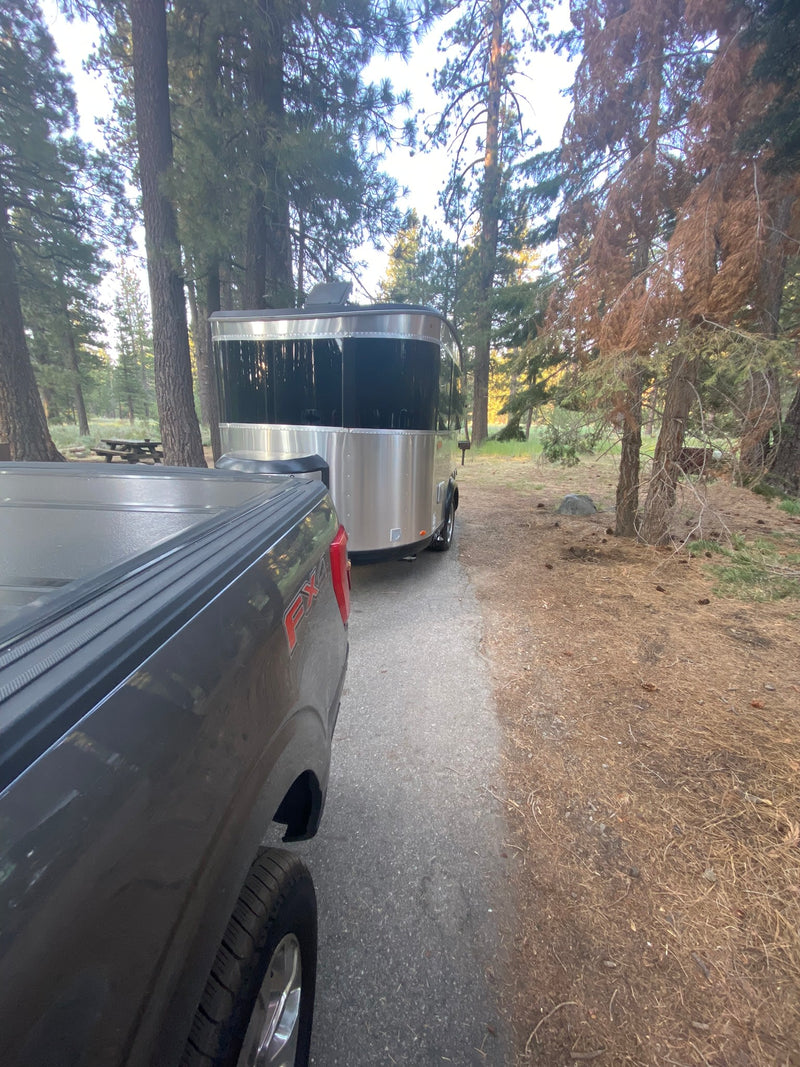 An RV rental travel trailer hitched to a pickup truck at a serene forest campground, with a picnic table in the distance. — photo 19