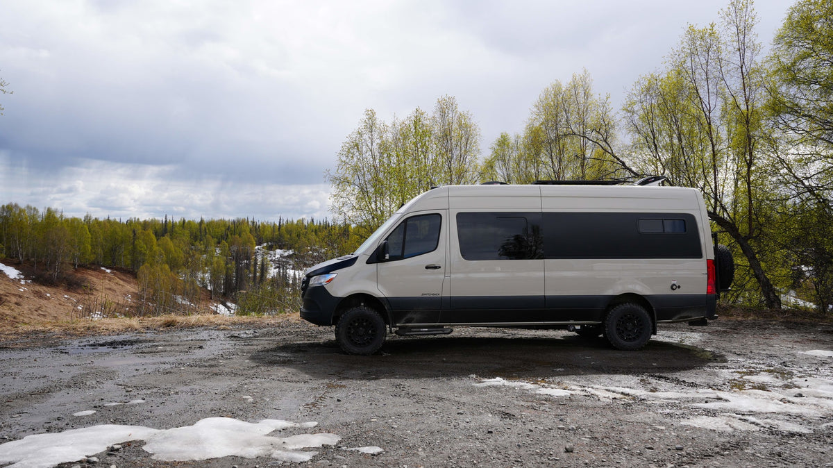 An off-road RV rental camper van on a muddy path overlooking a forest with melting snow. Ready for your nature adventure!|An RV rental