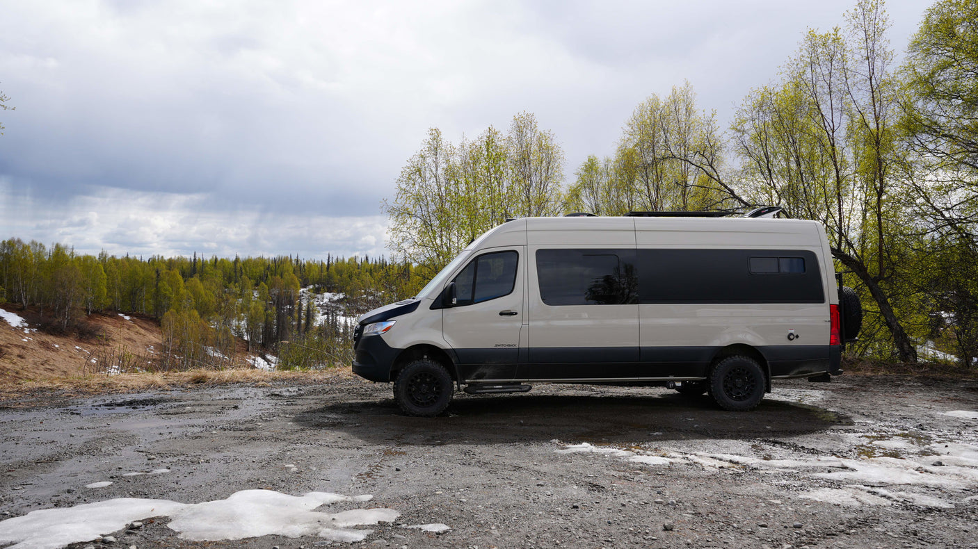 An off-road RV rental camper van on a muddy path overlooking a forest with melting snow. Ready for your nature adventure!