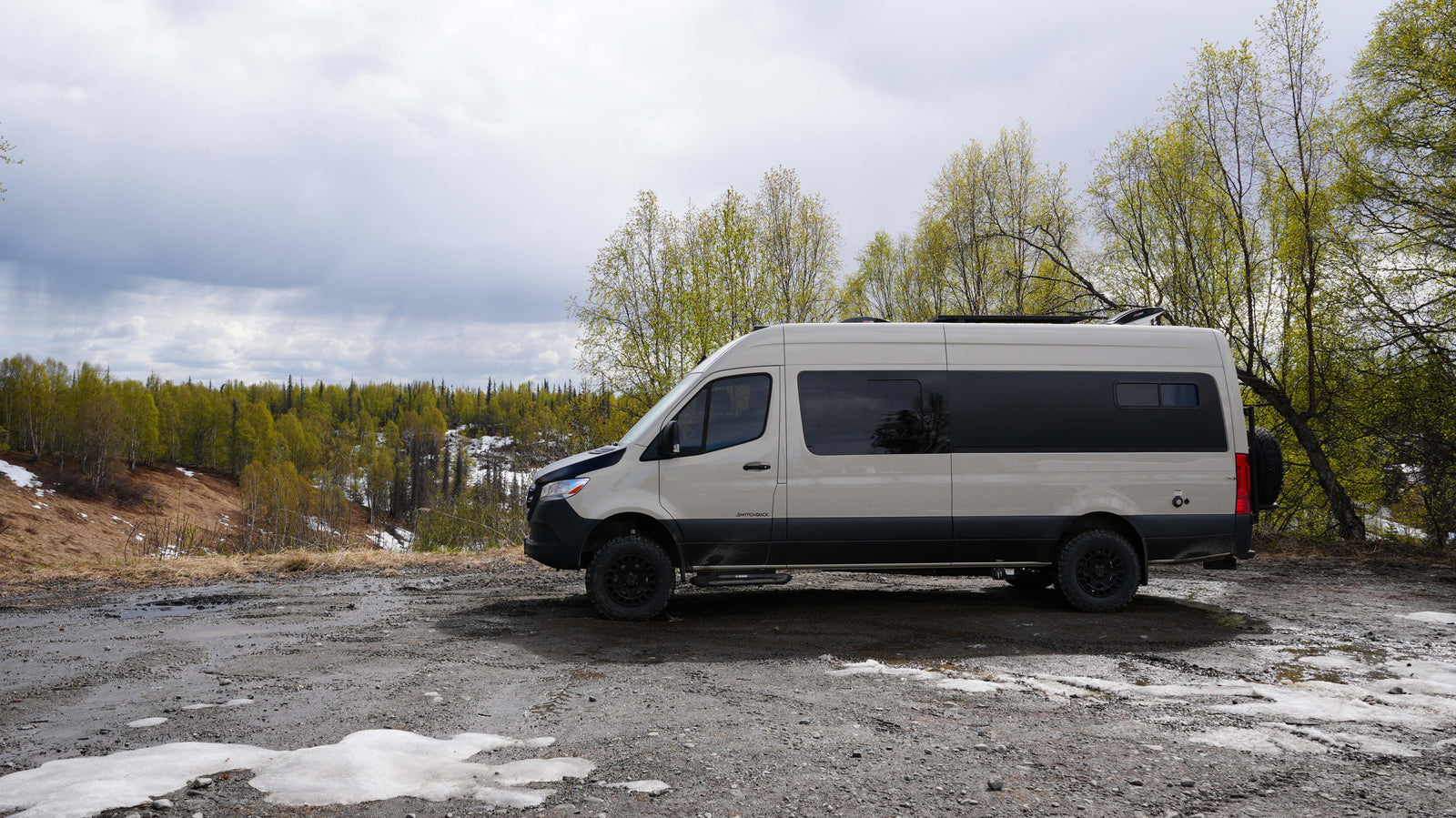 An off-road RV rental camper van on a muddy path overlooking a forest with melting snow. Ready for your nature adventure!