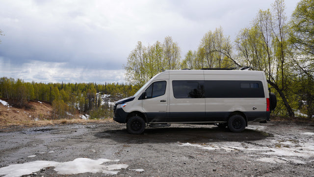 An off-road RV rental camper van on a muddy path overlooking a forest with melting snow. Ready for your nature adventure!