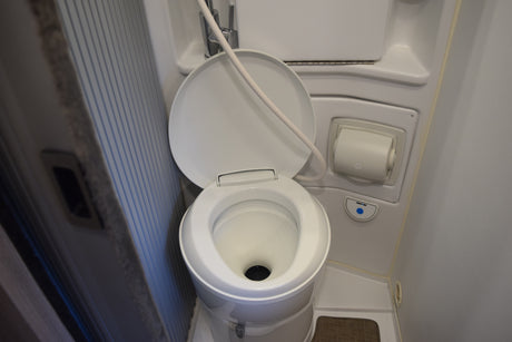 Compact white toilet with bidet/sprayer, TP holder, and Thetford flush in an RV rental bathroom.