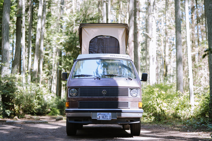 Front view of a Westfalia camper van, perfect for rv rental, parked in a sunny forest with its pop-top extended.