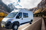 White RV rental van on a scenic mountain road with snow-capped peaks and autumn trees. Plan your adventure.
