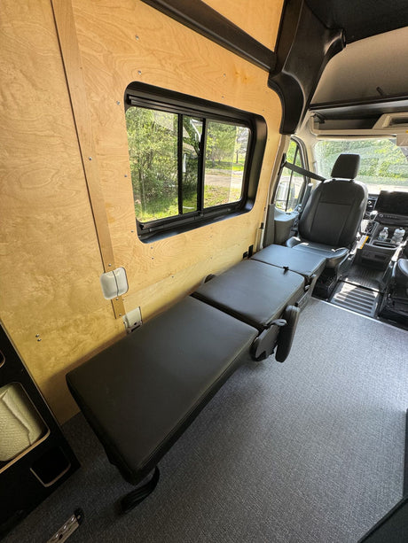 RV rental interior: Versatile black padded seating converts to a bed, set against warm wood walls and a large window.