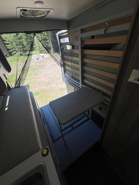 Inside an rv rental: versatile interior with a cozy bench, extendable table, and slatted bed frame looking out to nature.