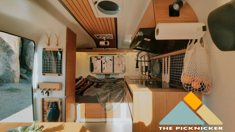 Cozy RV rental interior with a compact wood-paneled kitchen, comfy bed, and clever storage solutions for travel. — photo 3