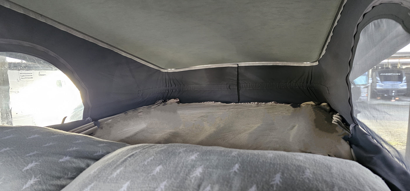 Cozy RV rental pop-top sleeping area, with a bed, pillows, and a window view of another RV at a campsite.