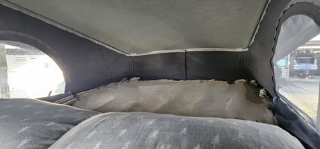 Cozy RV rental pop-top sleeping area, with a bed, pillows, and a window view of another RV at a campsite.