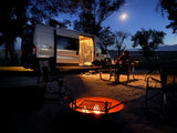Cozy RV rental camping night with a person at a picnic table, by a campfire & camper van under moonlight.