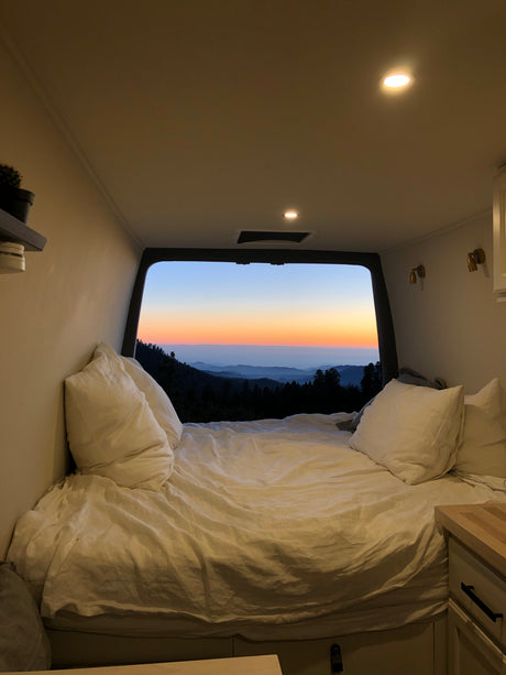 Cozy RV rental interior with a bed and stunning mountain sunset view. Perfect for van life adventures!