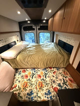 Spacious rv rental interior featuring a main bed with green duvet, a floral sofa-bed below, and storage for van life comfort.