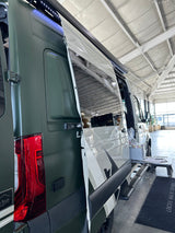 Custom dark green RV rental van with side door open, revealing interior features and an exterior setup under a white ceiling.