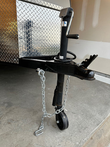 Close-up of an RV rental trailer's diamond plate box, hitch, and tongue jack with safety chains.