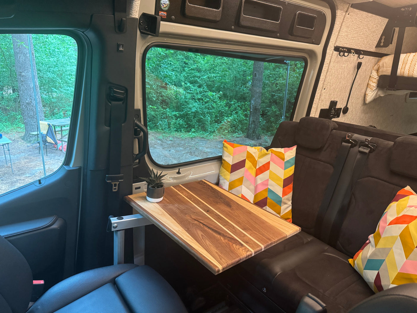 Cozy RV rental interior with a portable table, plush seating, and a scenic view of the forest campsite.