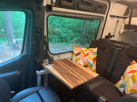 Cozy RV rental interior with a portable table, plush seating, and a scenic view of the forest campsite.
