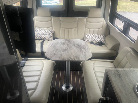 Spacious RV rental interior features cream leather seating, an octagonal table, and large windows.