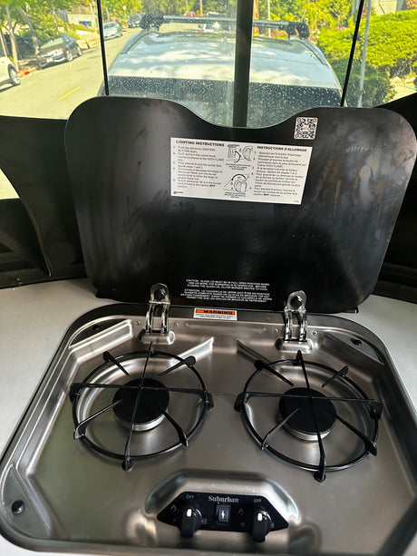 Compact RV rental gas stove: 2-burner Suburban unit with integrated glass lid & lighting instructions for your adventure.