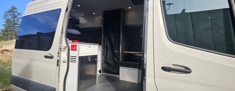 Inside an RV rental van: custom interior with compact kitchen, fridge, storage, and sleeping area.