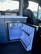 Open mini-fridge with freezer and shelves inside an RV rental camper van, perfect for road trips.