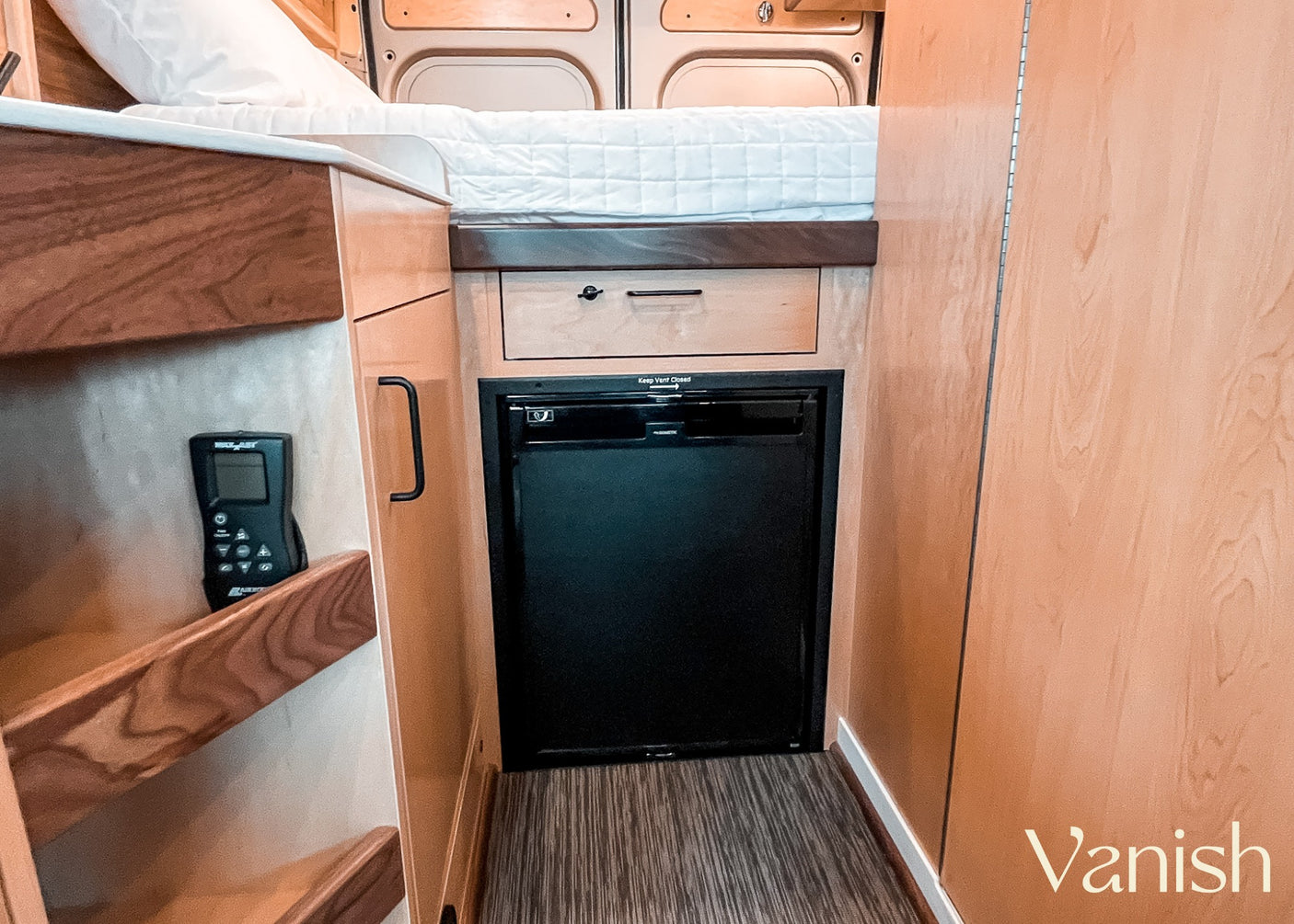 Compact RV rental interior featuring a cozy bed, integrated fridge, and control panel for comfortable travel.