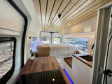Modern RV rental interior showcasing a cozy bed, kitchenette with wood counters, and a stylish wooden slatted ceiling.