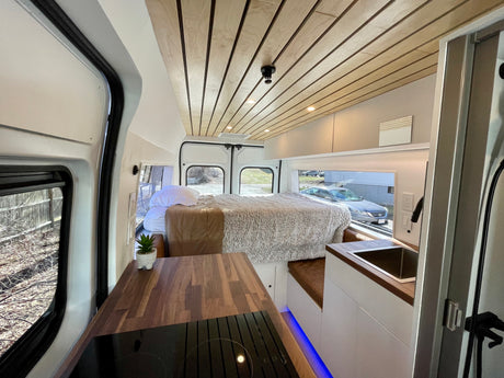 Modern RV rental interior showcasing a cozy bed, kitchenette with wood counters, and a stylish wooden slatted ceiling.