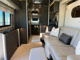 Step into this sleek rv rental featuring a comfy grey leather sofa, footrests, modern kitchen, and a window with a water view.