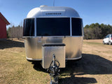 Front view of an Airstream rv rental: a shiny silver travel trailer parked on a grassy field with a red building nearby.