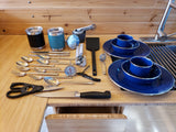 RV rental kitchen essentials: plates, cups, flatware, and various cooking tools neatly displayed on a wood counter.