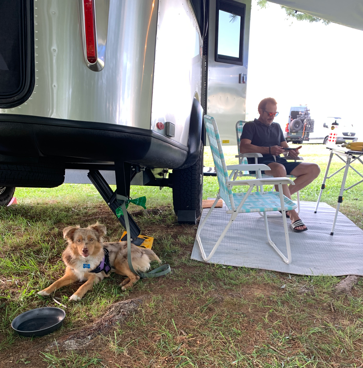 A man relaxes outside his RV rental with his dog at a campsite, enjoying the outdoor life.