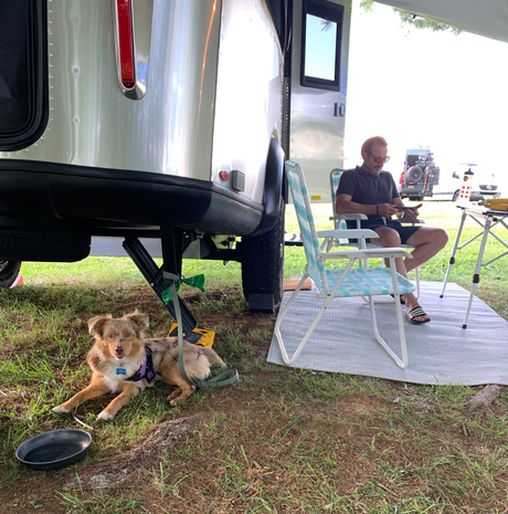 A man relaxes outside his RV rental with his dog at a campsite, enjoying the outdoor life.
