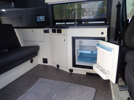 Spacious rv rental interior with a functional kitchen featuring an open fridge, comfy bench seating, and digital controls.