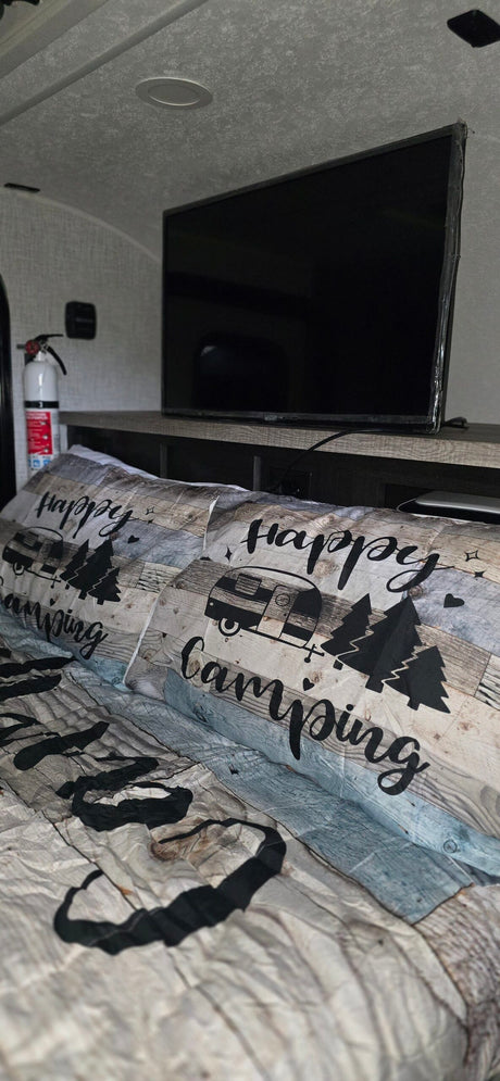 Cozy RV rental bedroom featuring "Happy Camping" bedding, a TV, and a fire extinguisher for safety. Perfect for your next adventure!