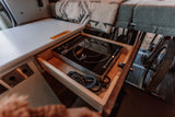 RV rental kitchen: a pull-out drawer reveals an induction cooktop. Cozy bed above, bike storage below.