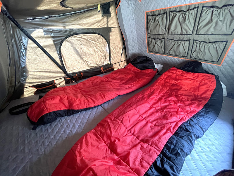 Inside a spacious RV rental: two red sleeping bags on a quilted bed, wall storage, and windows, ready for your camping travel. — photo 8
