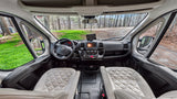 Spacious RV rental cockpit showing dashboard, steering wheel, quilted seats, and wooded view outside.