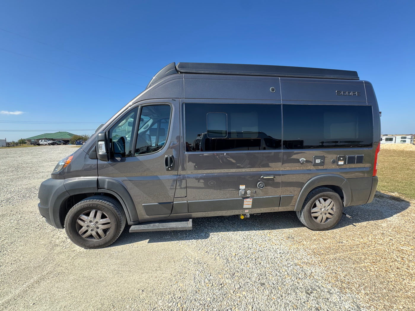 Grey Scope camper van, an RV rental, parked on gravel under a clear blue sky. Ready for your next road trip. — photo 2