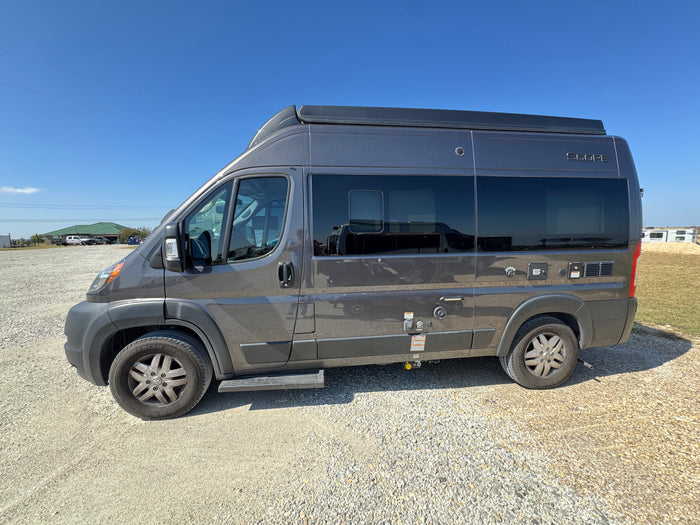 Grey Scope camper van, an RV rental, parked on gravel under a clear blue sky. Ready for your next road trip.