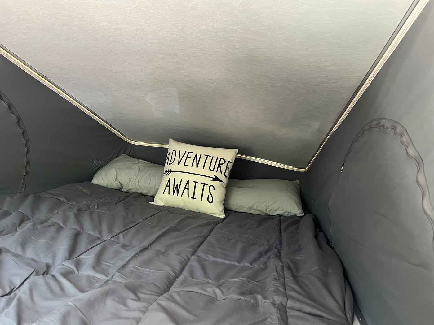 Interior of an RV rental: a comfortable bed with an 'Adventure Awaits' pillow, inviting travel and rest. — photo 15