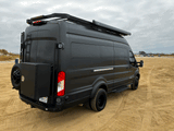 Black Ford Transit RV rental camper van on sand, with roof rack & awning.