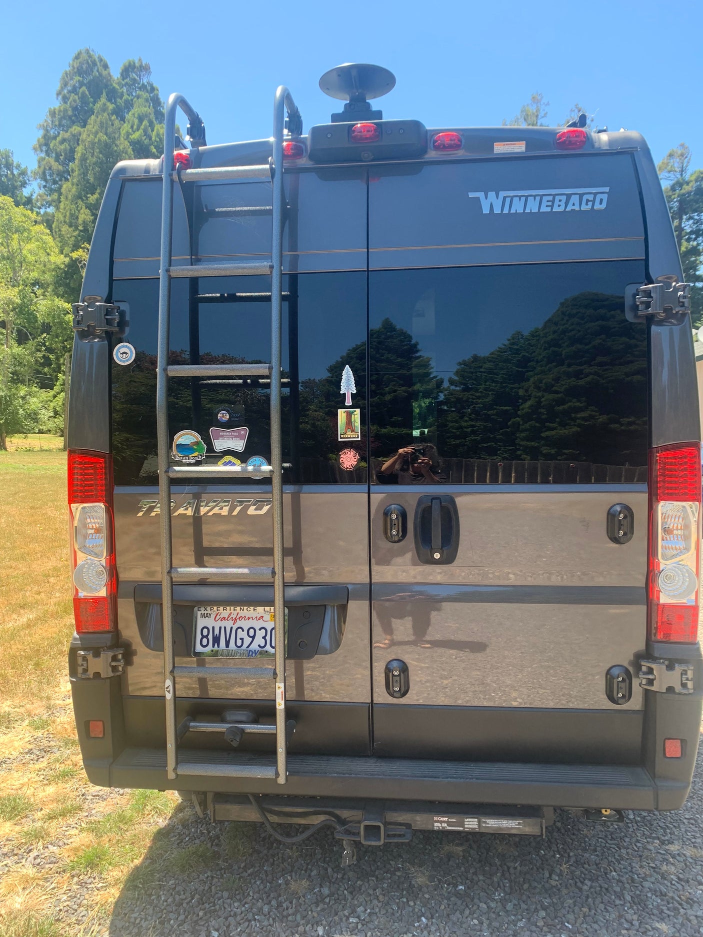 Rear view of a Winnebago Travato RV rental, featuring a ladder, California plate, and travel stickers from past road trips.