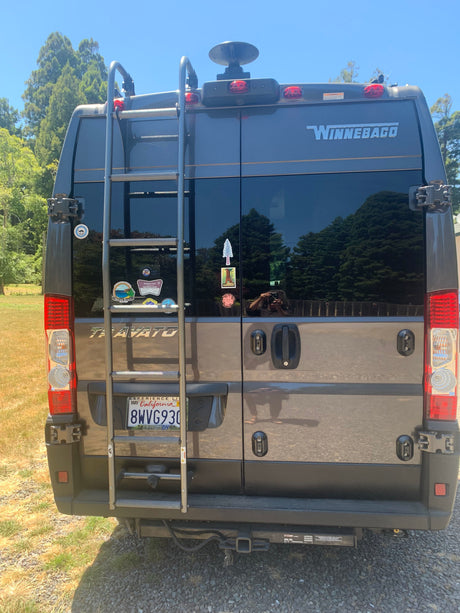Rear view of a Winnebago Travato RV rental, featuring a ladder, California plate, and travel stickers from past road trips.